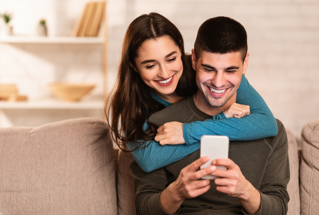 Lovely couple using cell phone sitting on sofa